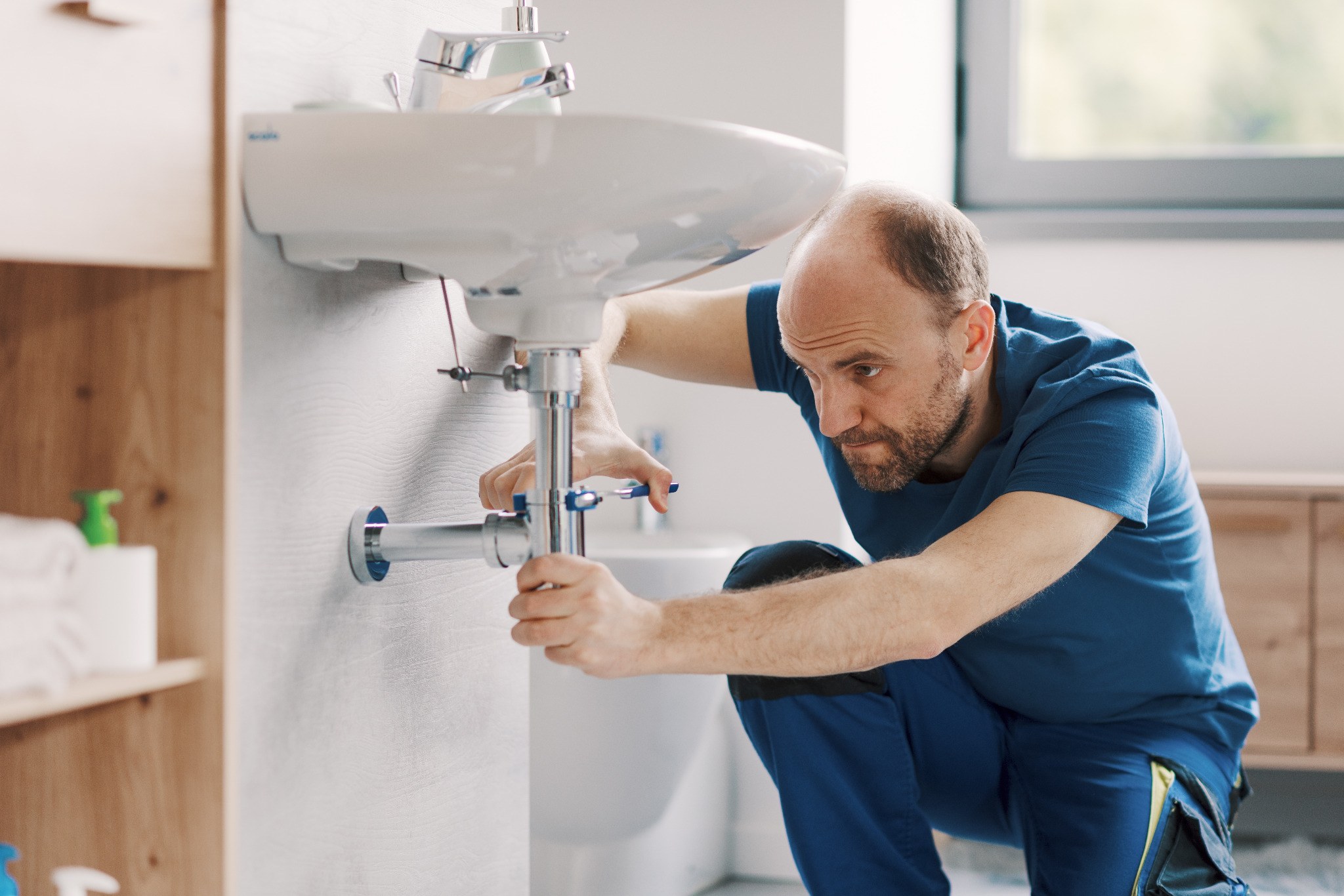 Plumber repairing pipework below a bathroom basin